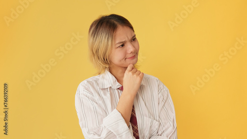 Young woman dressed in shirt and tie, thinks something isolated on yellow background in studio