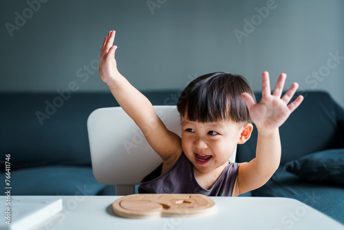 child winning a game with both hands raised. Child playing and completing a wooden puzzle.