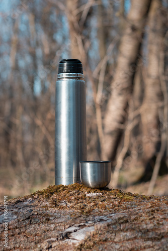 coffee in the forest. coffee cup on the ground. a thermos of coffee in the forest. spring landscape in the forest. a cup of tea in the forest. hot time with a thermos in the forest