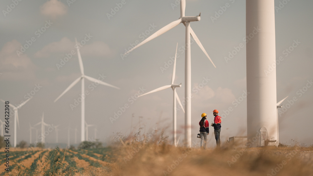 Young man and woman maintenance engineer team. two engineer operate wind turbine. Engineer and worker discussing on a wind turbine farm. Wind Turbine. Maintenance Workers. renewable energies.. - obrazy, fototapety, plakaty 