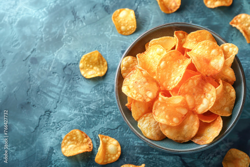 Crispy Golden Homemade Potato Chips. A bowl of freshly made golden potato chips, showcasing their crisp texture and homemade appeal on a rustic blue textured background.