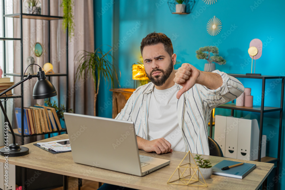Fototapeta premium Dislike. Upset Caucasian business man at home office room showing thumbs down sign gesture, expressing discontent, disapproval dissatisfied bad work feedback. Displeased guy freelancer. Lifestyle