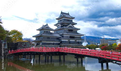 The scenery of the Matsumoto Castle with the red wooden bridge is in the foreground, in Nagano prefecture, Japan,  during the beginning of the fall season.