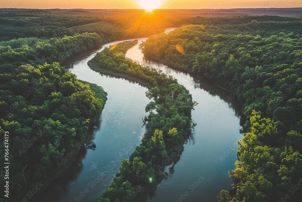 The sun sets over a serene river winding through a forested landscape
