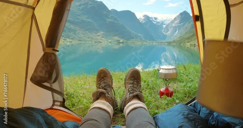 Feet, camping tent and relaxing on vacation, travel and mountain view on morning in nature. Person, drinking coffee and lazy on holiday, hot beverage and tea on outdoor adventure at lake or river pov photo