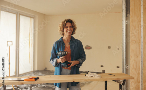Woman holding a drill gun while renovating her home's kitchen