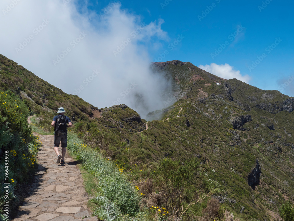 Man hiker in hat walking at paved footpath, hiking trail PR1.2 from Achada do Teixeira to Pico Ruivo mountain, the highest peak in the Madeira, Portugal.