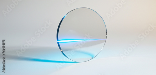 An optically clear, thin fu ll glass circle, seen from a side angle with a rotated perspective. a blue line of light shines through the circle and stands against a pristine white background © Malik Zohaib