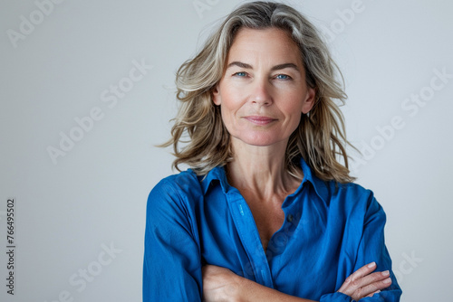 Attractive middle aged woman with folded arms with blue shirt isolated on solid white background.