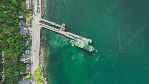 Aerial View of Docked Ship at the Pier Surrounded by Water. The top-down shot shows a ship docked at a long pier extending into emerald waters, capturing the tranquility of a seaside landscape.