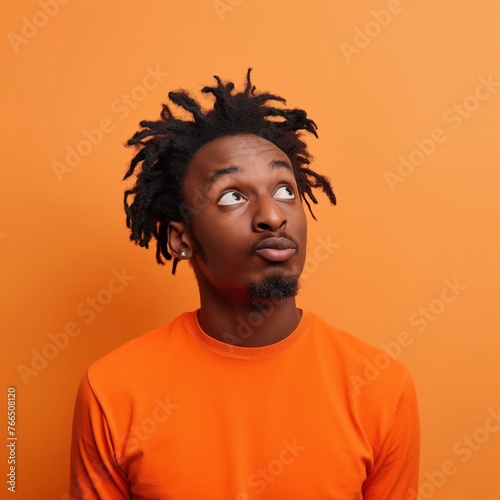 An isolated portrait of an African American man with a confused and perplexed mind, wearing an orange top, on an orange background with copy space.