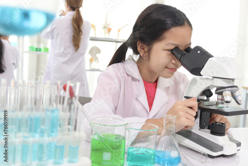 Cute young scientist schoolgirl in lab coat looks through microscope for study microbiology in laboratory. Student girl child use lab equipment doing science experiment. Kid learning science education