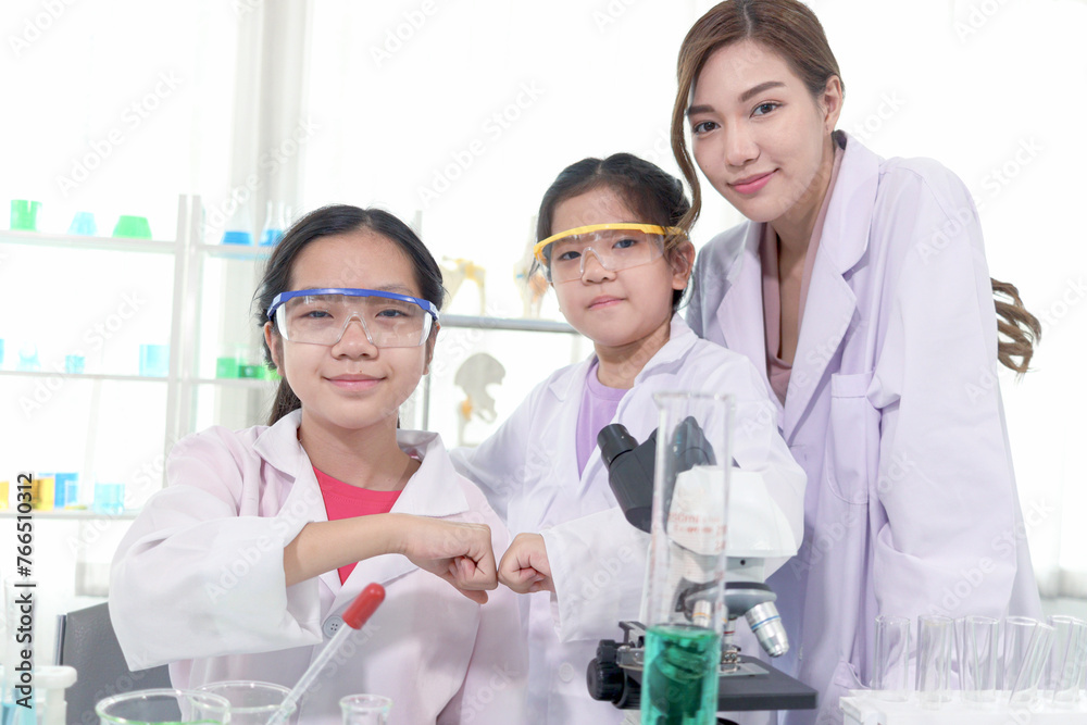 Young Asian student schoolgirls in lab coat bumping fists together to celebrate success of science experiment at laboratory. Student with female scientist teacher. Kid learning science education. Young Asian student schoolgirls in lab coat bumping fists together to celebrate success of science experiment at laboratory. Student with female scientist teacher. Kid learning science education.