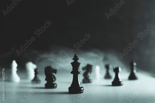 Close up of chessmen on chessboard, with the focus on the centrally placed black king, smoke and haze in the picture