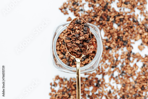 granola in a golden spoon on a glass jar, next to a strip of granola on a white background