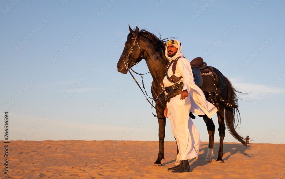 Saudi man  in traditional clothing in a desert with his horse