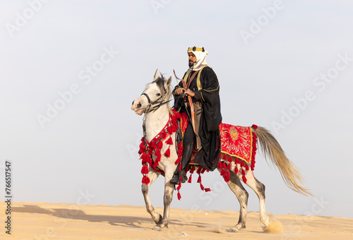 Saudi Man with his white stallion in a desert, shooting an arrow