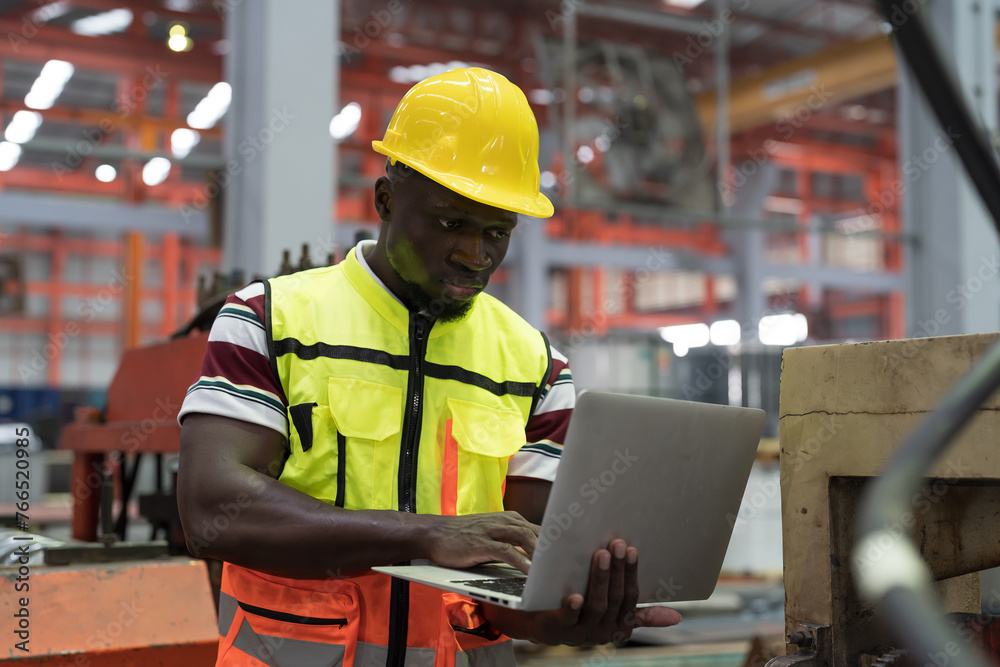 Male factory worker working with laptop computer in the industry factory. African American worker inspecting quality of manufacturing process in plant Male factory worker working with laptop computer in the industry factory. African American worker inspecting quality of manufacturing process in plant