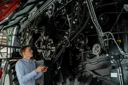 Serviceman with digital tablet next to combine harvester with open hood