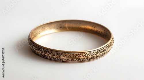 Tribal-inspired brass bangle featuring intricate etched patterns, standing out against the pristine white surface with its unique design.