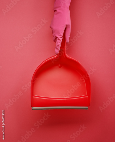 Hand in pink glove holding dustpan against pink background