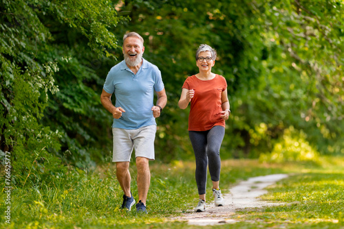 Joyful senior couple jogging together along park path