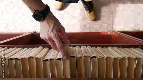 Close-up of many old books on a book shelf and a man's hand takes one photo