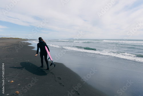 Happy surfer woman in wetsuit with surfboard go to winter surfing in ocean. Adventure Extreme travel sport concept
