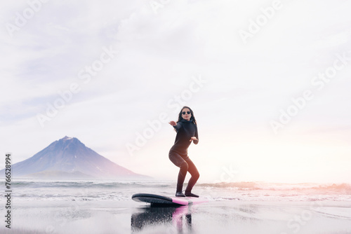 Extreme surfer woman in wetsuit with surfboard go to winter surfing in Atlantic ocean Kamchatka Russia. Adventure travel sport concept