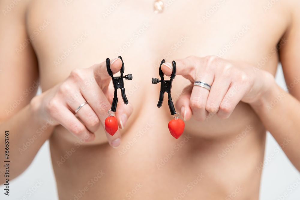 Close-up view of sexy caucasian topless slim woman wearing clips with red hearts on index fingers. Breast is covered with hands. Soft focus. Fetish accesories theme. - obrazy, fototapety, plakaty 