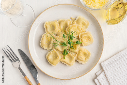 Top view of italian traditional Ravioli pasta stuffed with mozzarella cheese with green fresh pea microgreens served on plate with tableware, olive oil, napkin and glass of white wine on wooden table