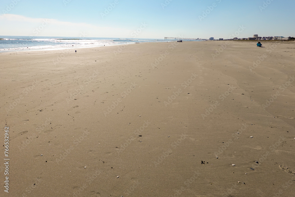 Very large smooth deserted beach by the ocean with a long pier in the background