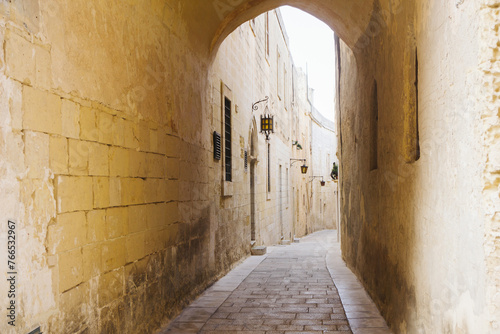 Ancient stone architecture. Narrow street pavement tunnel. Tiny streets of Malta downtown. City center od Mdina. Yellow color building walls. Arch alley cityscape.