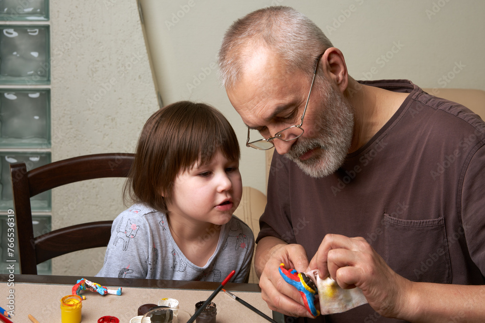 Joint leisure time of grandfather and granddaughter. They paint a clay ...