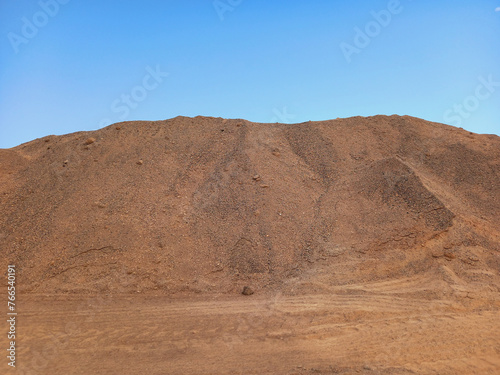 Volcanic landscape. Desert area with stones, rocks and sandstone and silhouette of volcano slopes on the horizon under blue sky. Landscapes and extreme nature.