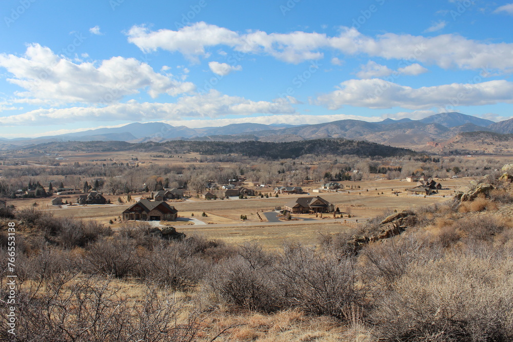 A winter view of countryside west of Devil's Backbone in Larimer County with blue sky and puffy white clouds.  Brown grasses and scrub bushes with rocky outcroppings and clouds.