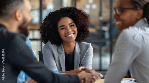 Business ethics and etiquette. Gender and ethnic diversity at work. Smiling young African-American woman shaking hands with negotiation partner, sitting at desk with male teammates in company meeting photo