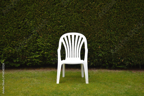 White chair in front of a hedge in a garden