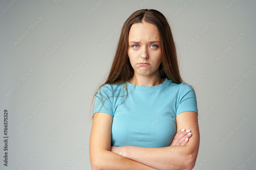 Portrait of sad displeased offended young woman in blue T-shirt on gray background Portrait of sad displeased offended young woman in blue T-shirt on gray background