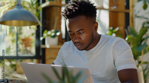 An African American man wearing a white T-shirt is using a laptop.