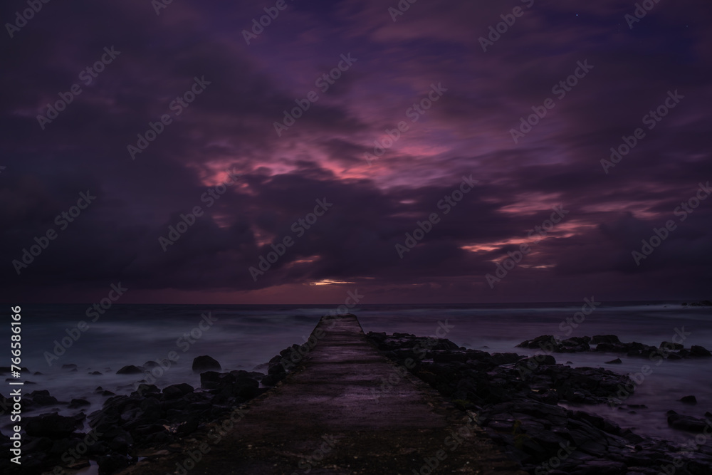 Obraz premium Long exposure view of sunrise from a pier at La Cambuse beach which is located in the south of Mauritius island 
