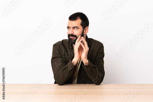 Caucasian man with beard in a table scheming something.