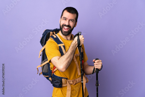 Caucasian handsome man with backpack and trekking poles over isolated background celebrating a victory
