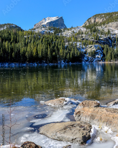 Ice forms on Bear Lake in Colorado.  Trees in the foreground of Hallett Peak in the Rocky Mountains.  Ice on Bear Lake with boulders in the foreground. photo