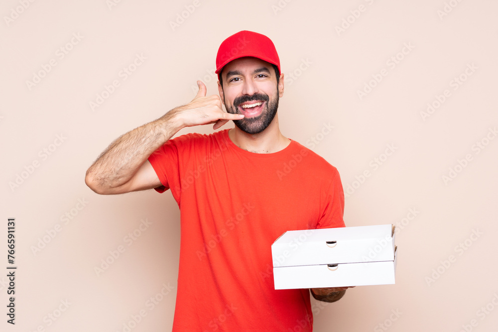 Young man holding a pizza over isolated background making phone gesture. Call me back sign Young man holding a pizza over isolated background making phone gesture. Call me back sign
