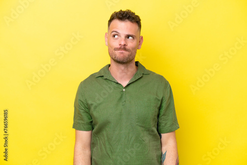Young caucasian handsome man isolated on yellow background having doubts while looking up