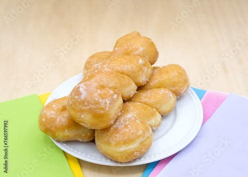 White porcelain plate with glazed twist donuts on a light wood table with colorful napkins on each side.