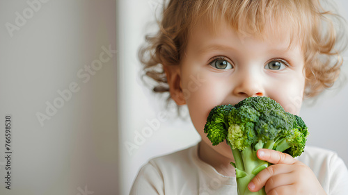 child with broccoli in hand in white room