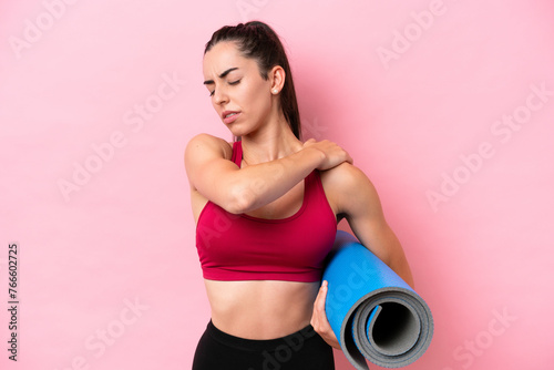 Fototapeta Naklejka Na Ścianę i Meble -  Young sport caucasian woman going to yoga classes while holding a mat isolated on pink background suffering from pain in shoulder for having made an effort