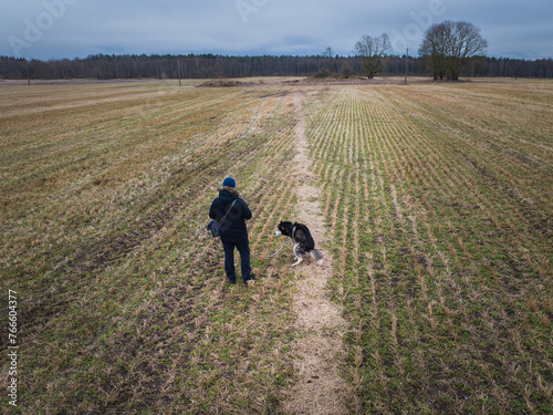 A man walks with a husky dog ​​that sat down to poop in a field in the spring, photo from a drone.